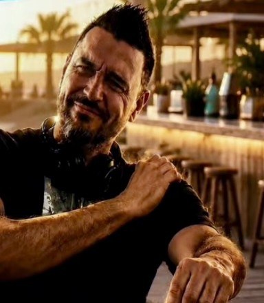 DJ L0BSTER sonriendo junto a la cabina de mezclas en un beach club al atardecer